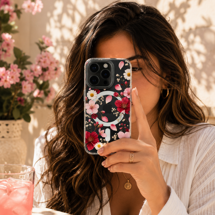 Clear MagSafe iPhone case with pink and red cherry blossoms, white daisies, baby’s breath and scattered flower petals.