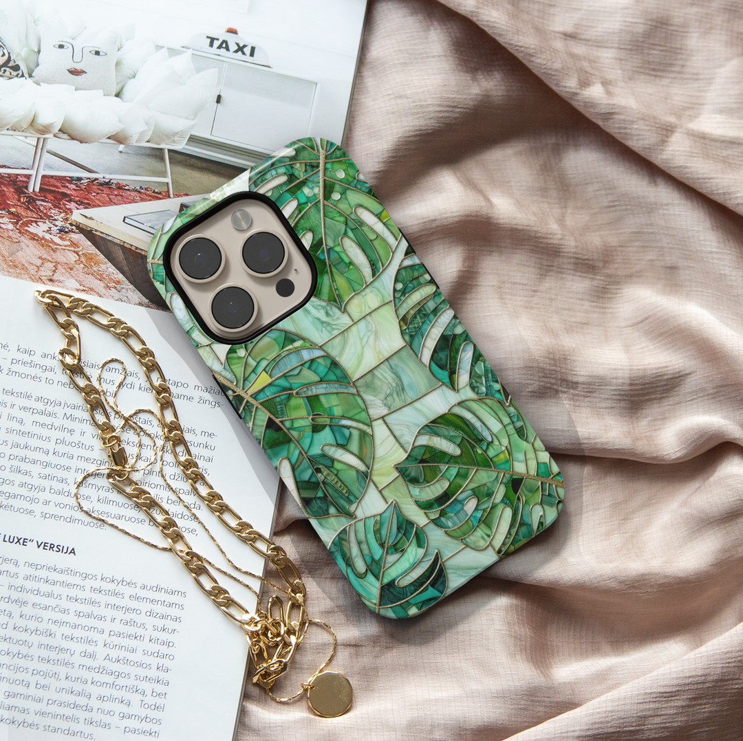 Green stained glass iPhone case featuring layered monstera leaves in emerald, jade, and sage botanical mosaic artwork.