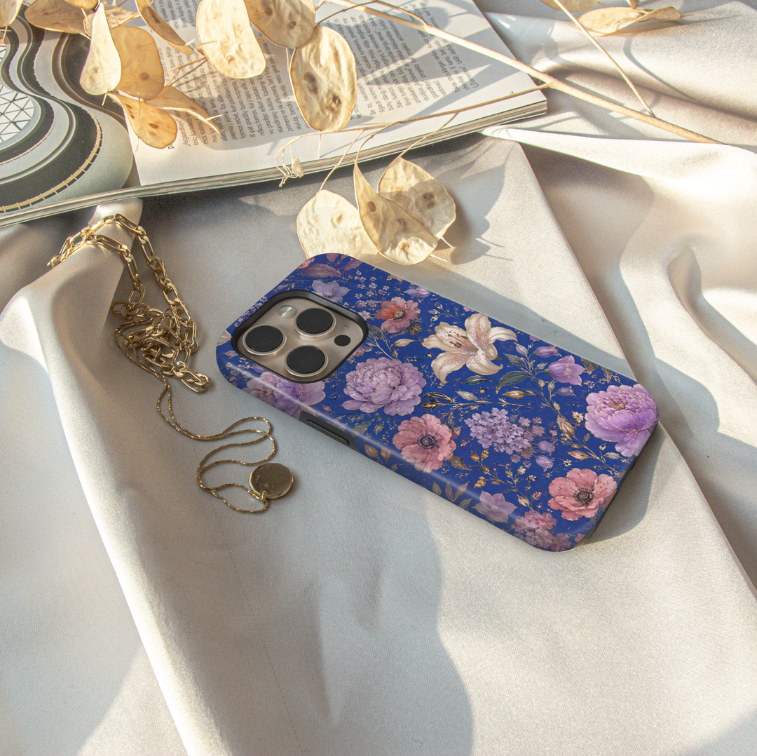 Electric Bloom iPhone case featuring vibrant coral, pink and orange flowers with green leaves on a cobalt blue background.