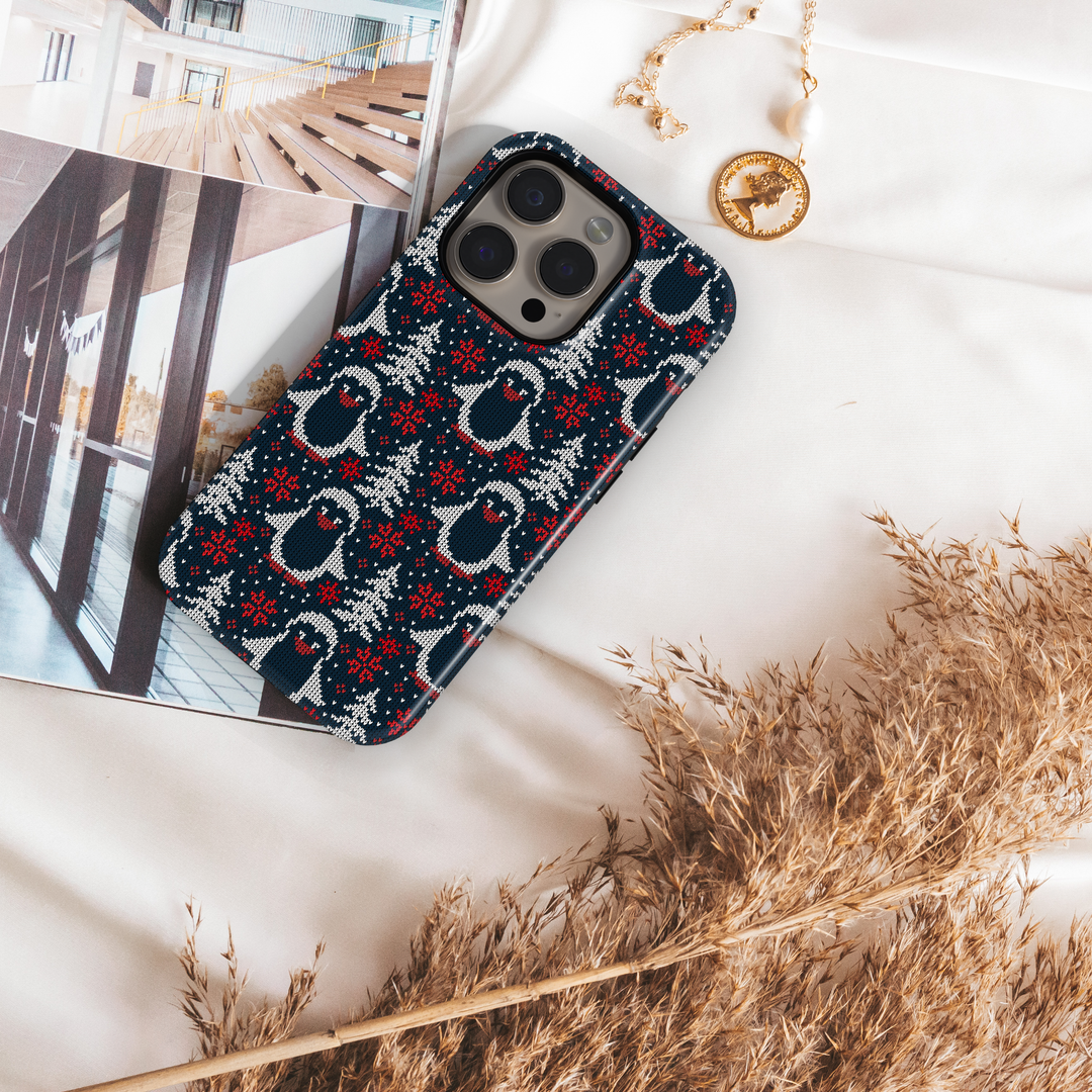 Navy blue Christmas phone case with white knitted penguins, red snowflakes, and winter trees sweater pattern