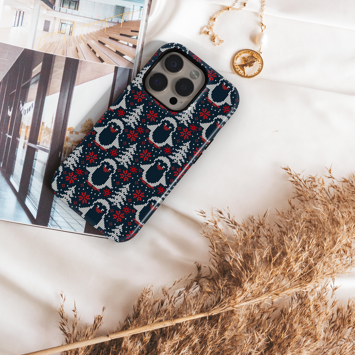 Navy blue Christmas phone case with white knitted penguins, red snowflakes, and winter trees sweater pattern